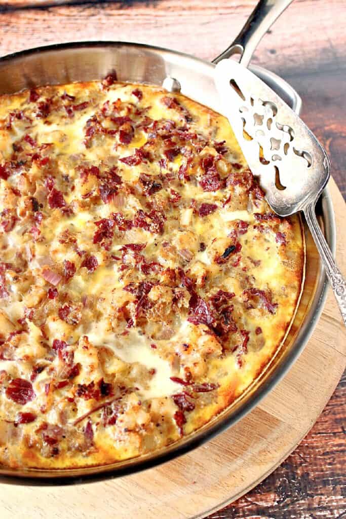 A vertical overhead photo of a Corned Beef Hash Fritatta in a silver skillet with a silver pie server.