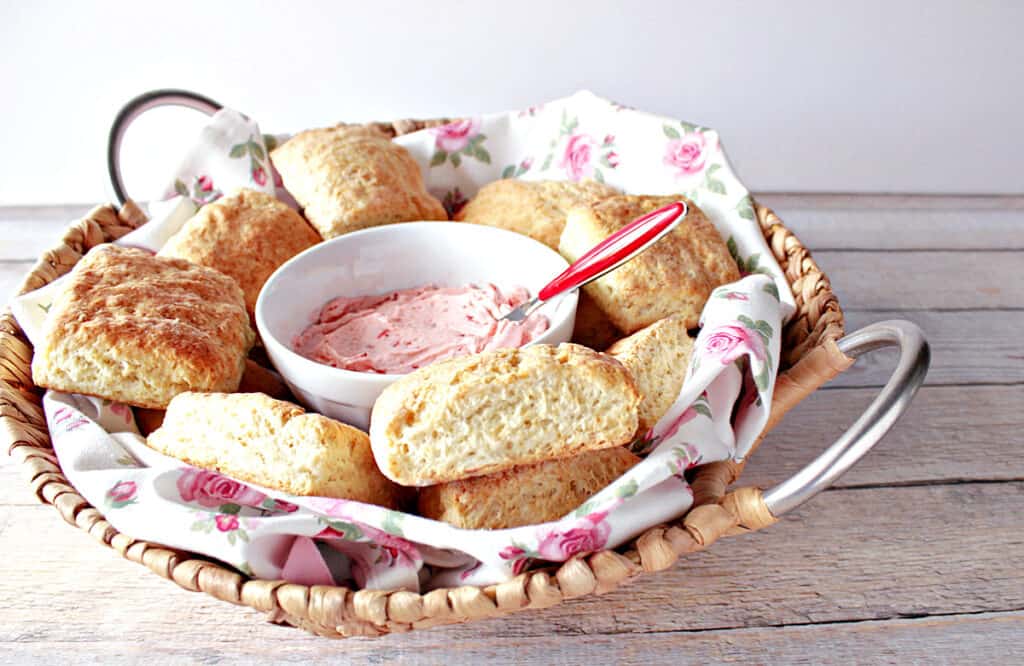 A pretty basket with silver handles filled with a pretty napkin along with Cream Cheese Biscuits and some strawberry butter.