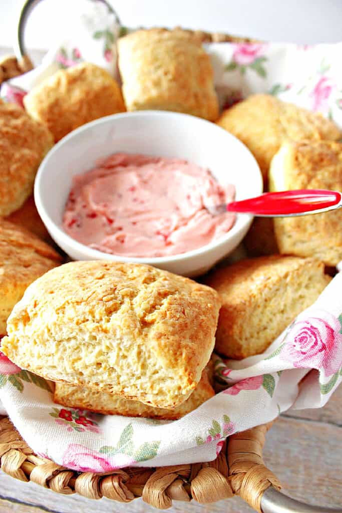 A vertical closeup of a basket of Cream Cheese Biscuits with a bowl of strawberry butter in the center. 