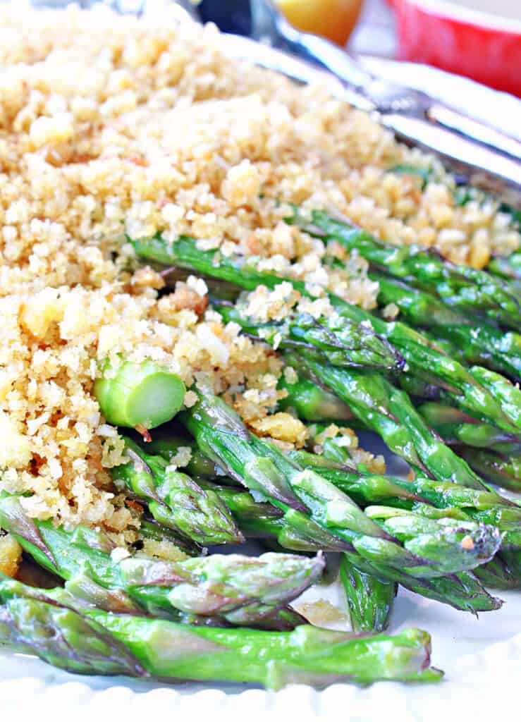 A super closeup vertical image of cooked asparagus on a platter covered in seasoned breadcrumbs.