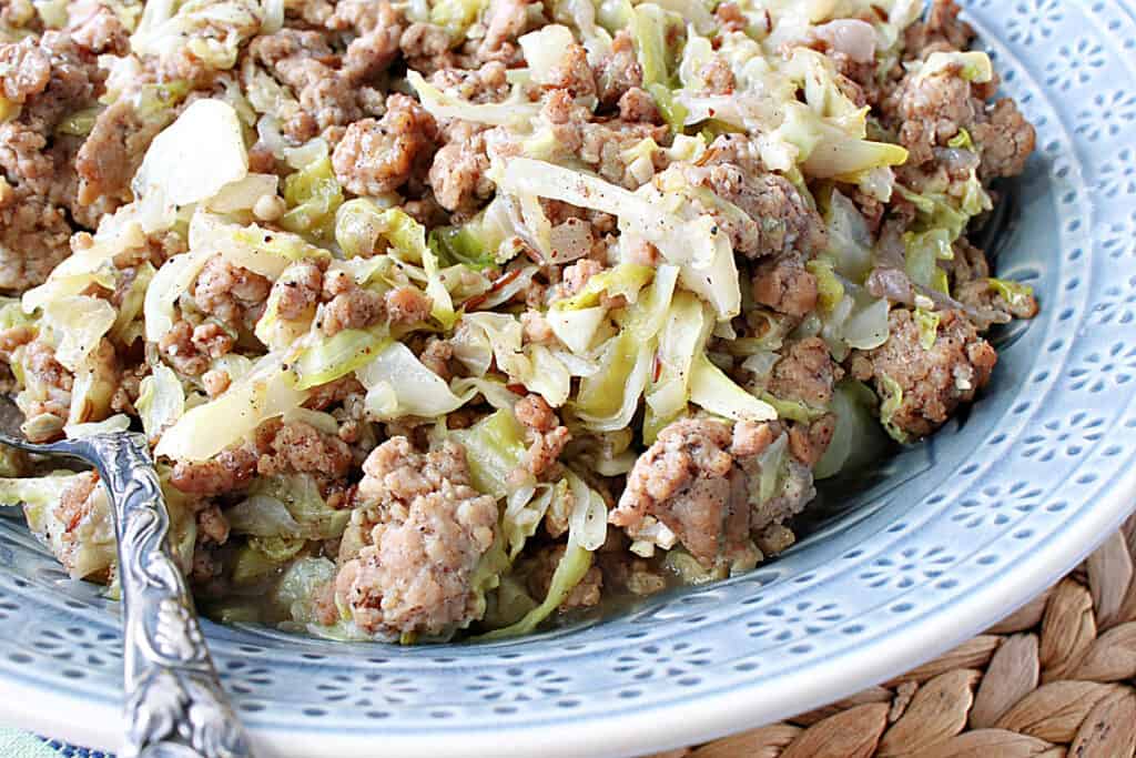 An offset closeup photo of Pork and Cabbage in a blue bowl with a serving spoon.