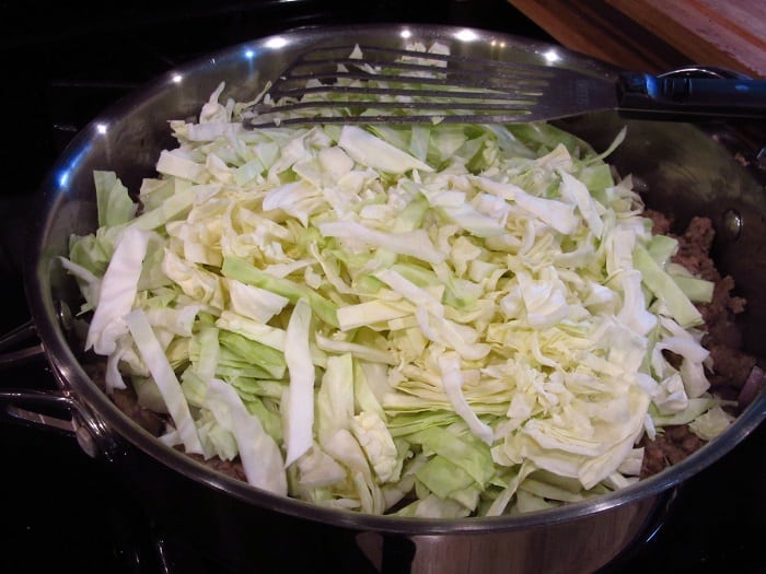 Fresh cabbage added to a skillet with ground pork 
