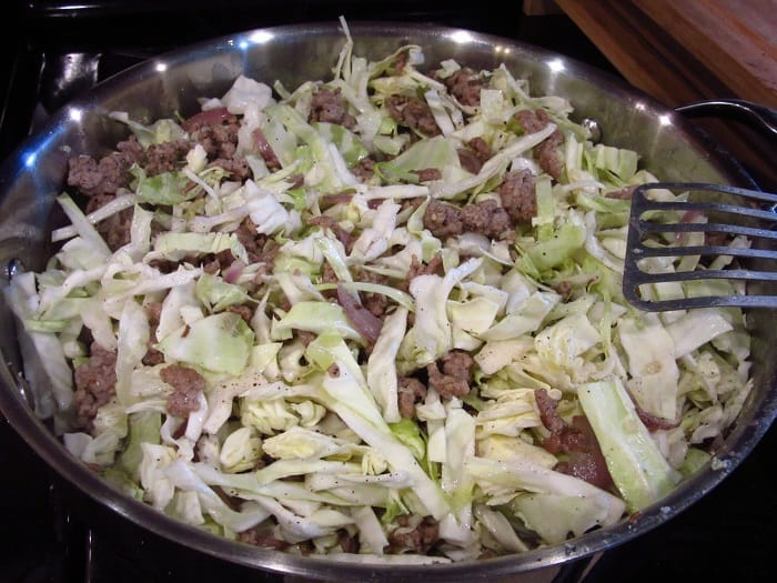 Ground pork and cabbage in a large skillet with a slotted spatula.