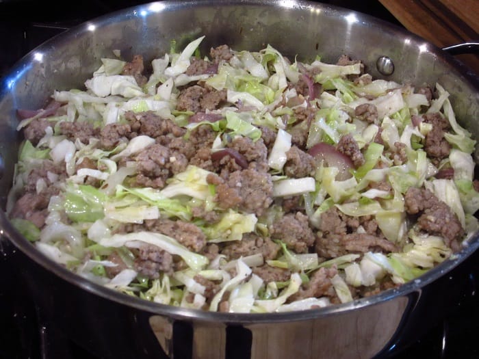 A mixture of ground pork and cabbage in a large skillet.