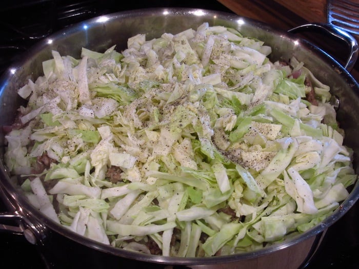 Salt and pepper in a skillet with sliced cabbage.
