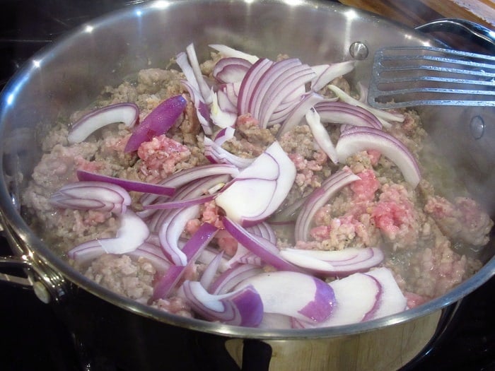Ground pork and red onion slices in a skillet.