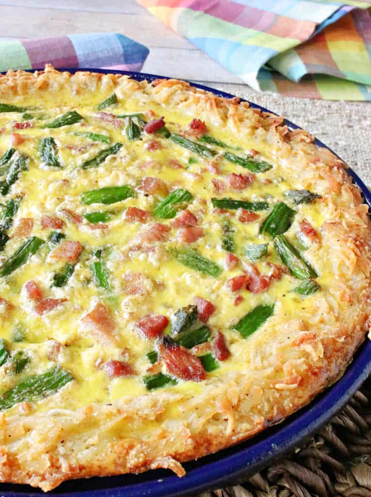 A vertical offset closeup photo of a Ham and Asparagus Quiche with a hash brown potato crust.