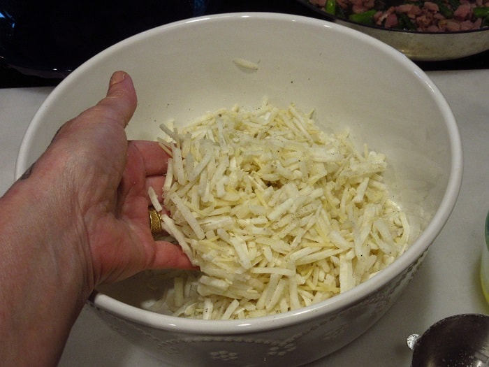 A hand mixing up frozen hash brown potatoes in a bowl.