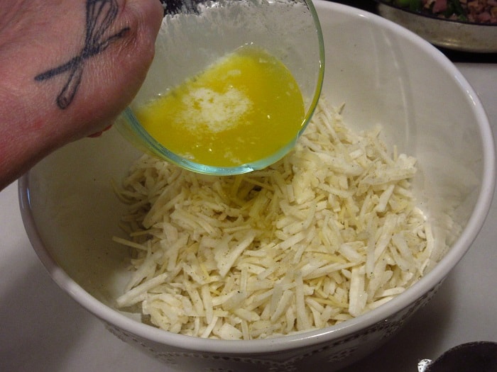 Melted butter being poured into a bowl with frozen hash brown potatoes.
