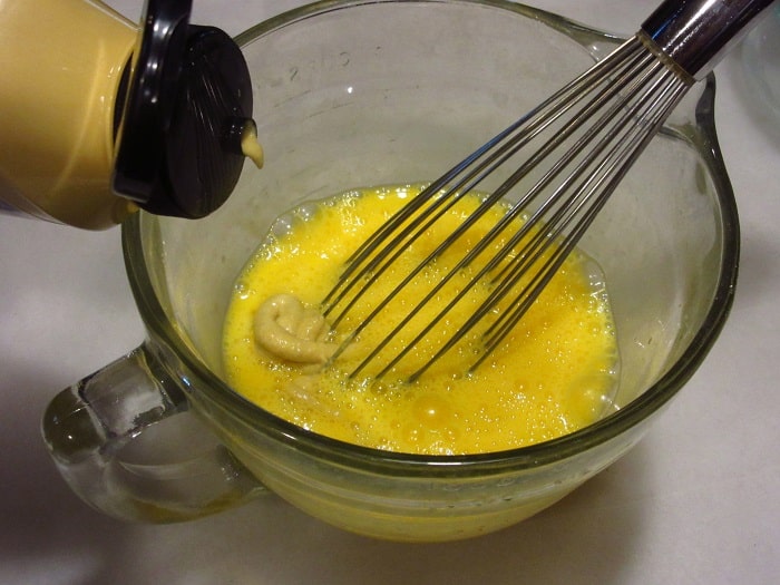 Dijon mustard being added to eggs in a bowl.