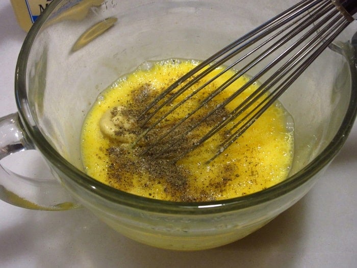 A whisk with eggs and seasonings in a glass measuring bowl.