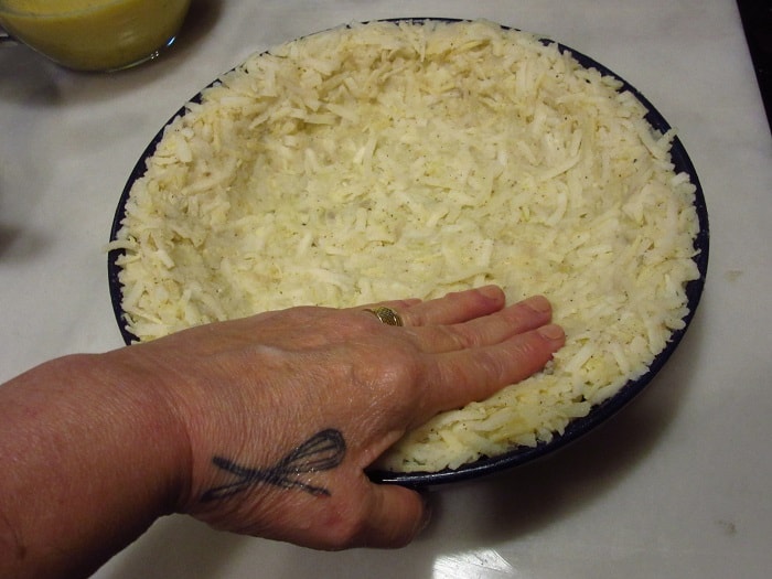 A hand pressing hash browns into place.