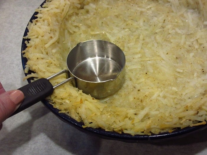 A measuring cup pressing a crust into a pie pan.