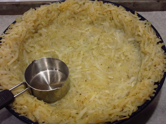 A measuring cup being used to form a hash brown crust for a quiche.