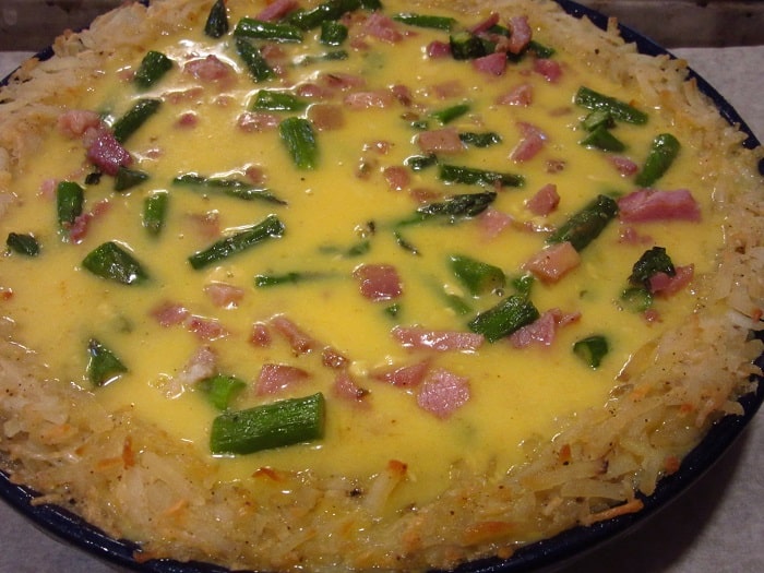 An unbaked quiche with a hash brown crust.