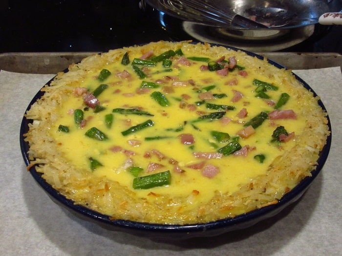 An unbaked quiche with ham and asparagus and a hash brown crust.