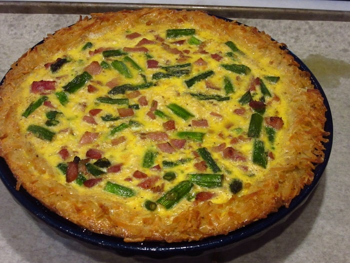 A golden brown Hash Brown Crust for a Ham and Asparagus Quiche on a baking sheet.