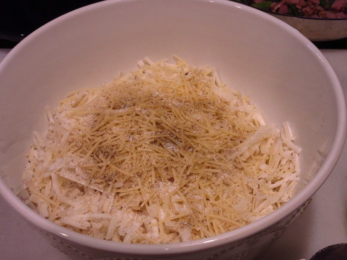 Potatoes cheese and seasonings in a bowl.