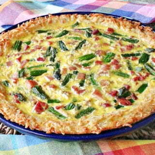 A Ham and Asparagus Quiche with a hash brown crust on a brown woven placemat with colorful napkins.