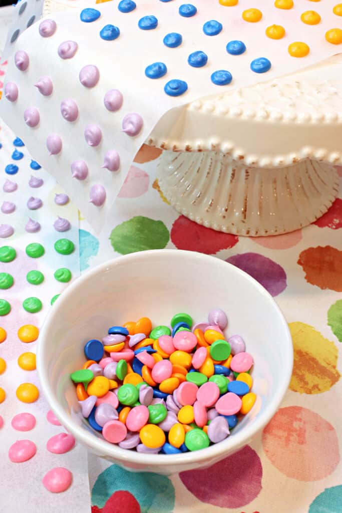 A vertical image of a small white bowl filled with bright colorful Homemade Candy Dots on a colorful polka dot napkin.