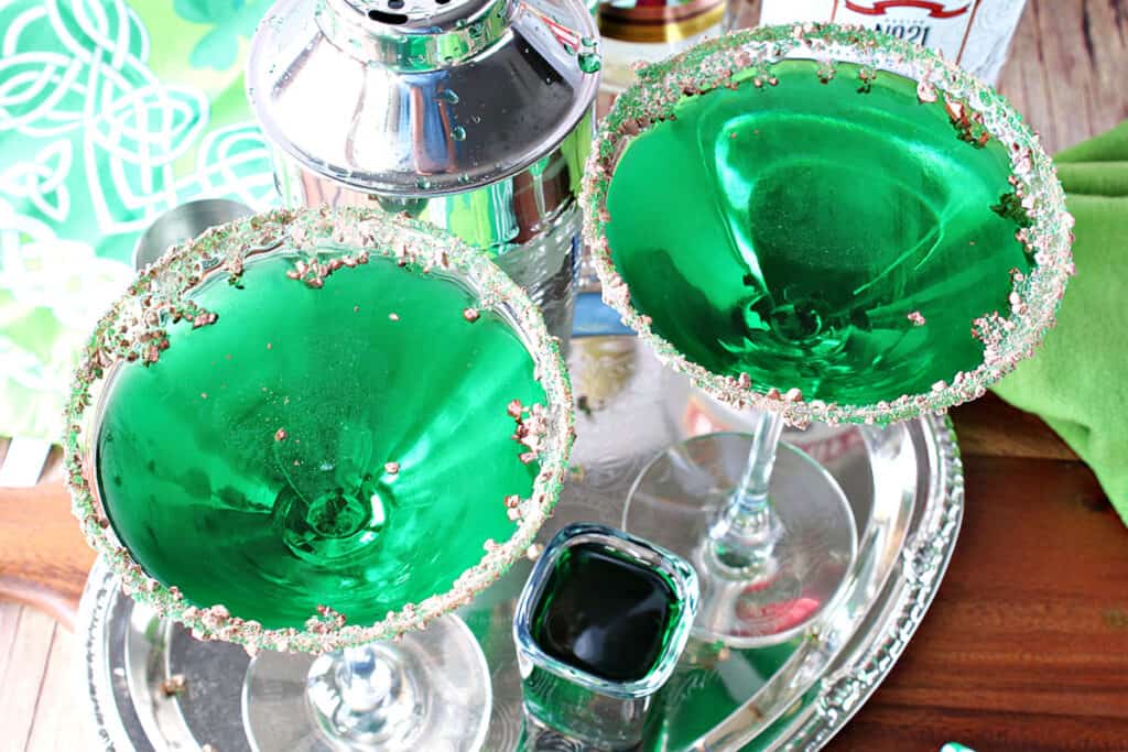 An overhead horizontal photo looking into two martini glasses filled with green Irish Grasshopper Cocktails on a silver platter.