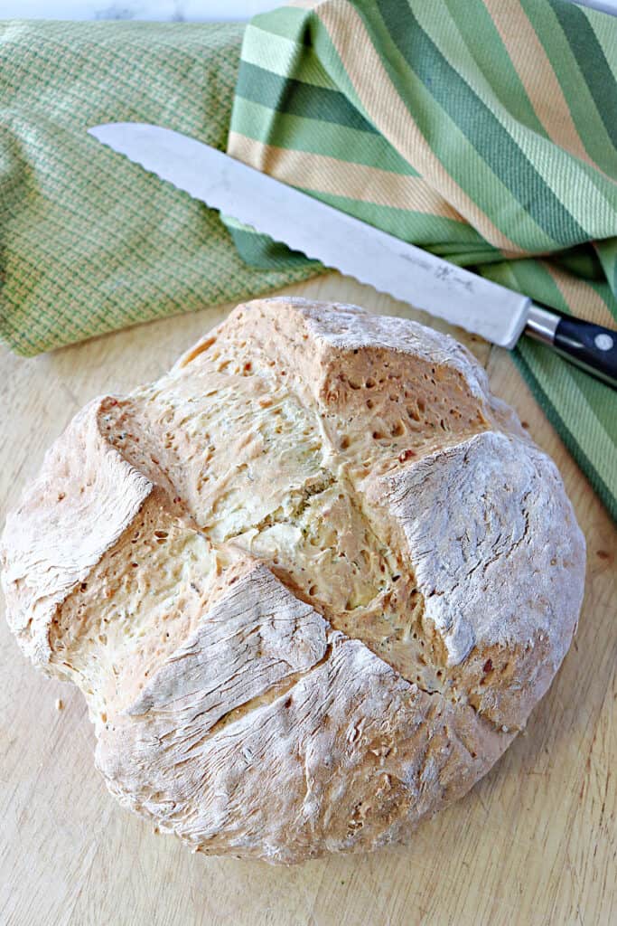 A loaf of Irish soda bread with dill and a serrated knife on the side. 
