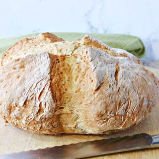 A whole loaf of Irish Soda Bread with Caraway and Dill on a wooden cutting board with a knife.