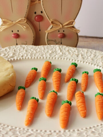 Homemade Marzipan Candy Carrots on a platter with bunnies in the background.