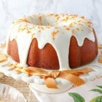 An Orange Bundt Cake with Bananas and Poppy Seeds on a white cake plate with an orange ribbon.