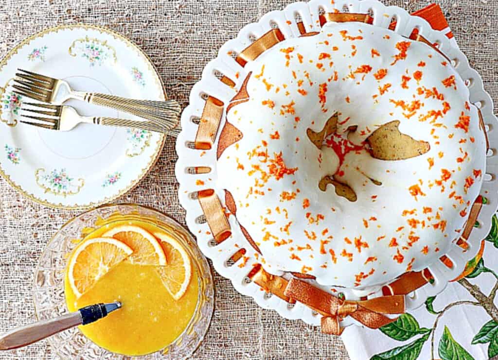 An overhead image of an iced Orange Bundt Cake with orange zest on top along with a bowl of orange curd on the side.