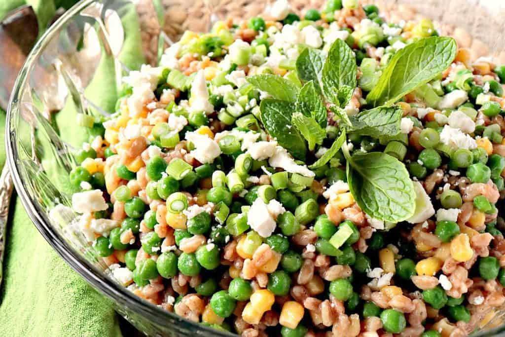 An offset horizontal photo of a Farro Salad with Peas and Scallions in a glass bowl with a green napkin and mint.