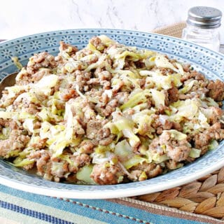 A blue bowl filled with Pork and Cabbage along with a serving spoon and a salt and pepper shaker in the background.