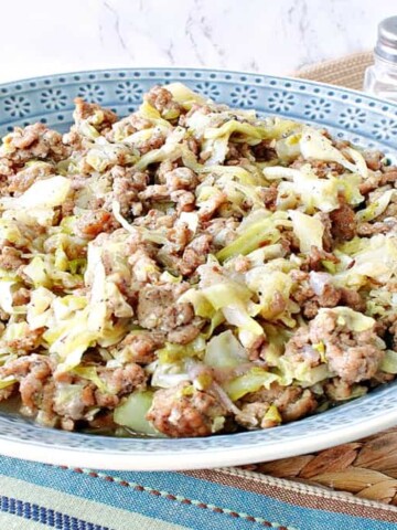 A blue bowl filled with Pork and Cabbage along with a serving spoon and a salt and pepper shaker in the background.