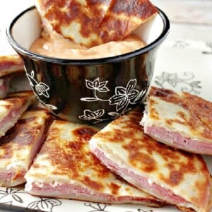 A triangle of a Rueben Quesadilla in a bowl of dipping sauce.