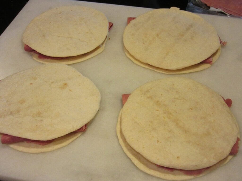 Four prepared but uncooked quesadillas on a marble countertop.