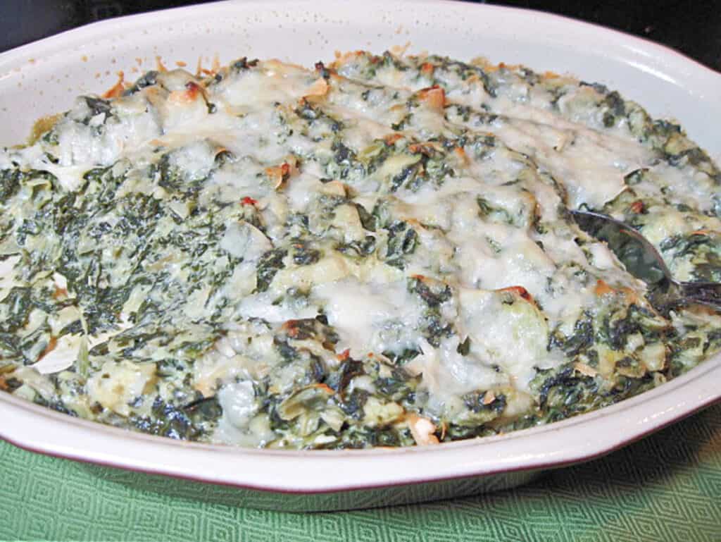 A oval baking dish filled with Spinach Artichoke Dip with melted cheese on top.