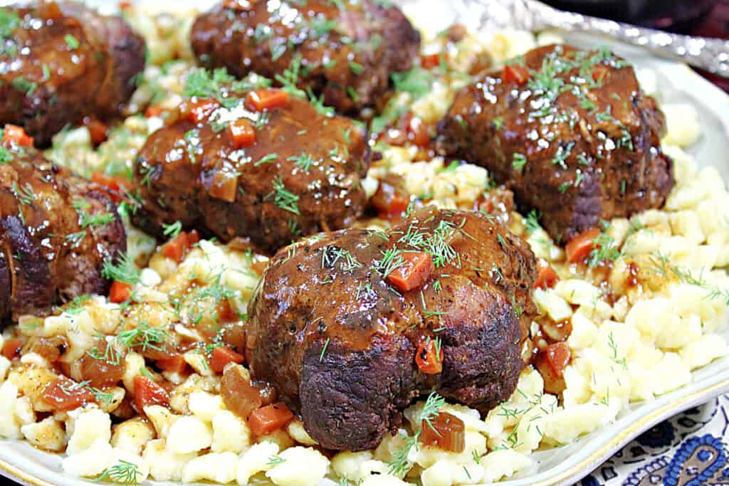 A closeup horizontal photo of German Beef Rouladen on a platter with gravy and fresh dill as garnish.