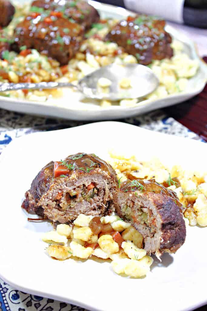 A vertical closeup of a Traditional German Beef Rouladen that has been cut in half on a plate with a full platter in the background.