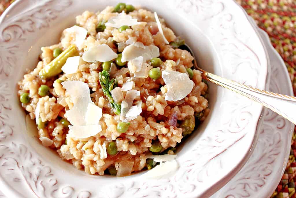 An offset horizontal photo of a pretty white bowl filled with Asparagus and Pea Risotto with Parmesan cheese shavings on top.