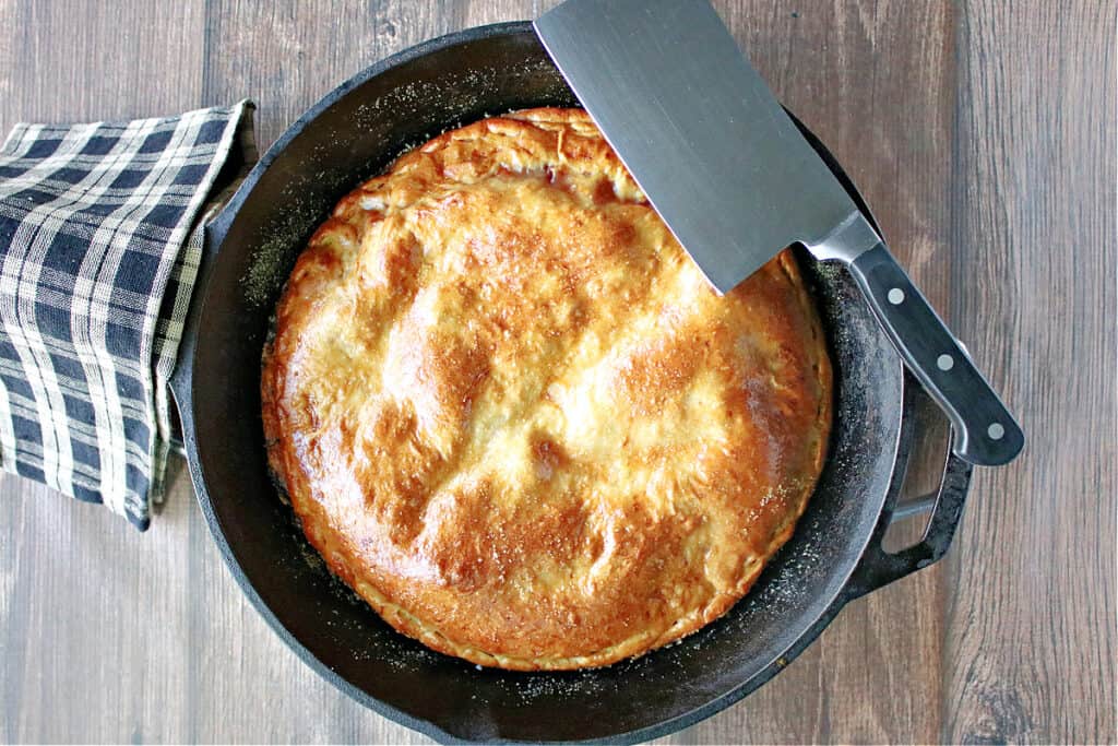 A direct overhead photo of a Double Crust Hawaiian Pizza in a cast iron skillet with a black and tan napkin and a clever on the side.