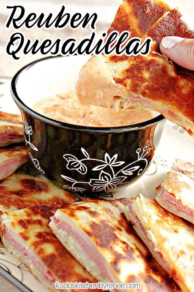  A vertical closeup of a hand holding a wedge of corned beef quesadillas dipped in sauce along with a title text overlay graphic in the corner.