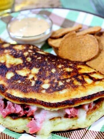 An Irish Boxty Sandwich with corned beef and Swiss cheese on a plaid plate.