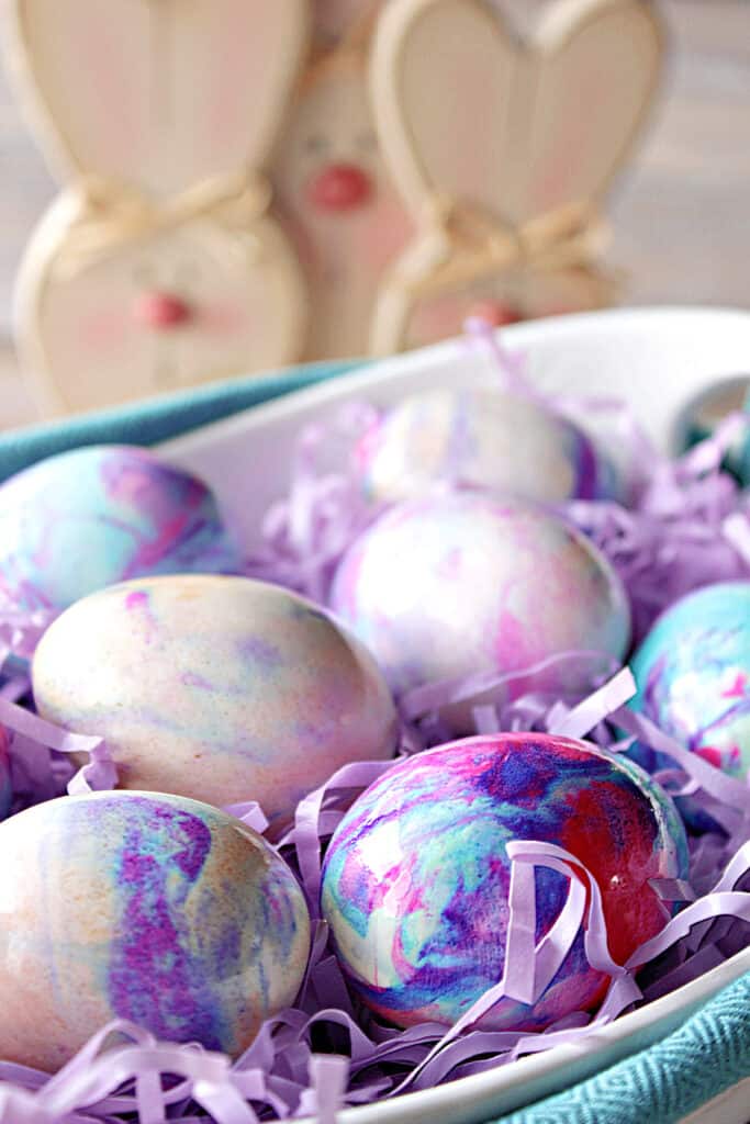A vertical closeup of swirled pastel colored Tie-Dye Easter Eggs with bunnies in the background.