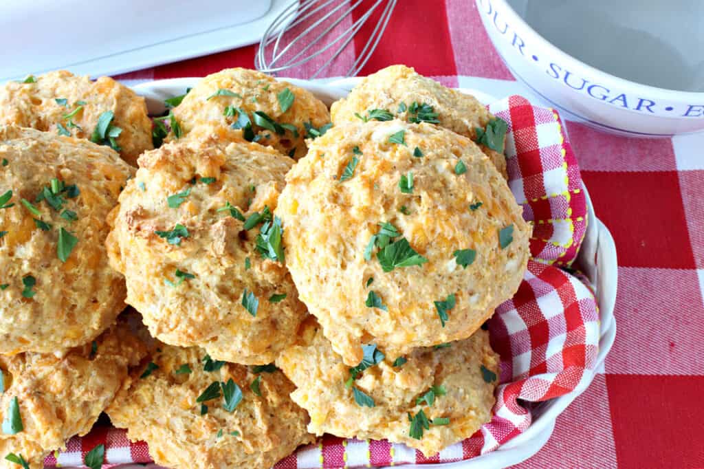 An overhead photo of a basket filled with Better Cheddar Bay Biscuits topped with fresh parsley and on a red and white checked napkin.