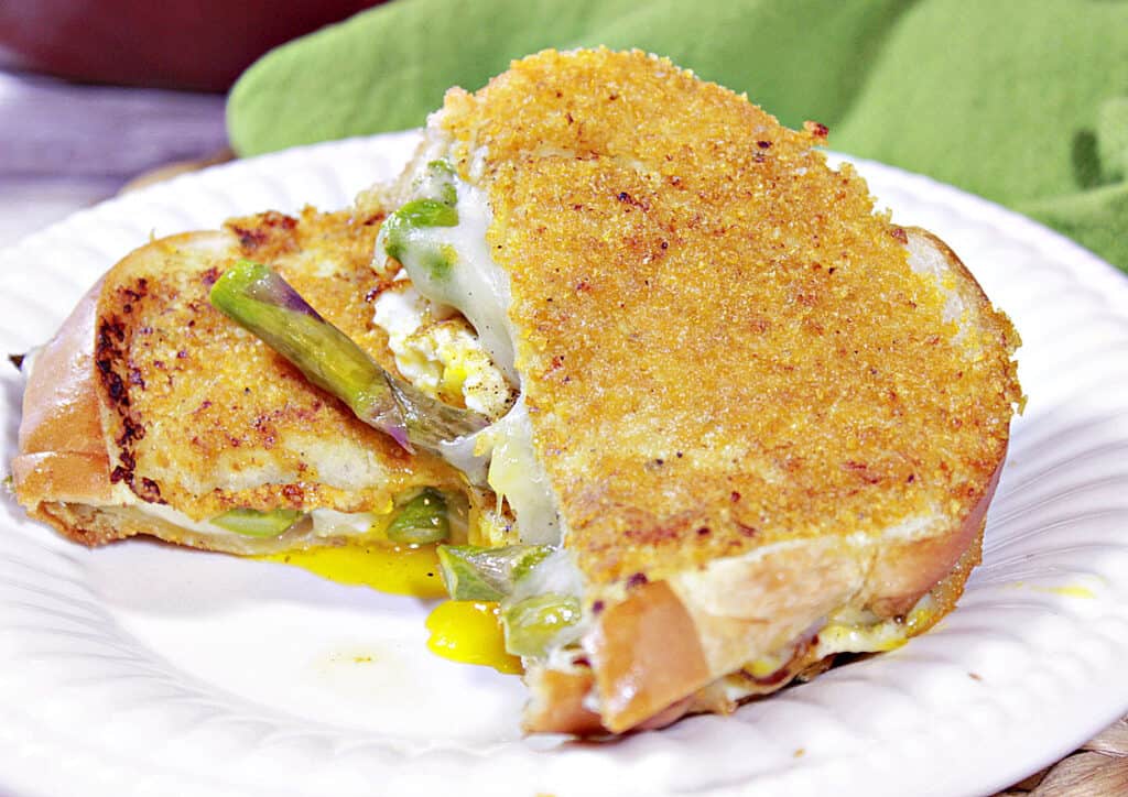 A sliced Grilled Cheese Breakfast Sandwich on a white plate with a green napkin in the background.