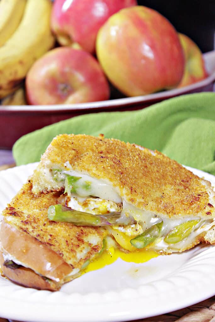 A vertical closeup image of a sliced in half Grilled Cheese Breakfast Sandwich with melted cheese and asparagus sticking out.