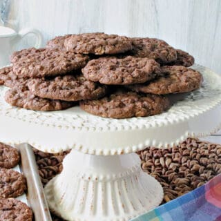 A white cake plate filled with Chocolate Oatmeal Cookies along with a colorful napkin in the foreground.