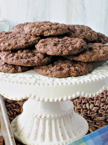 A white cake plate filled with Chocolate Oatmeal Cookies along with a colorful napkin in the foreground.