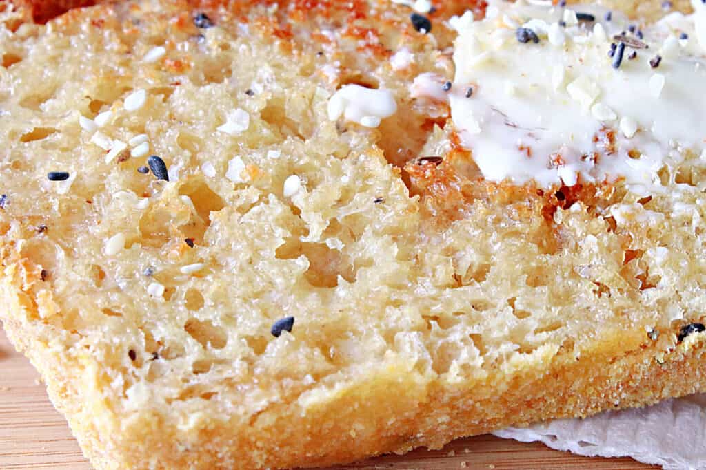 A super closeup horizontal photo of Everything English Muffin Bread with nooks and crannies and butter.