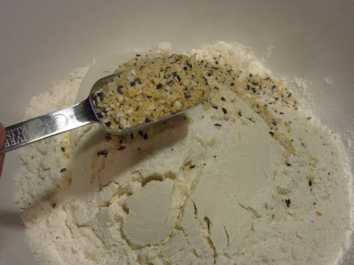 Everything seasoning blend being added to flour in a bowl.